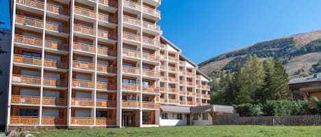 Un hotel de varios pisos con balcones, un patio cubierto de césped y montañas al fondo.