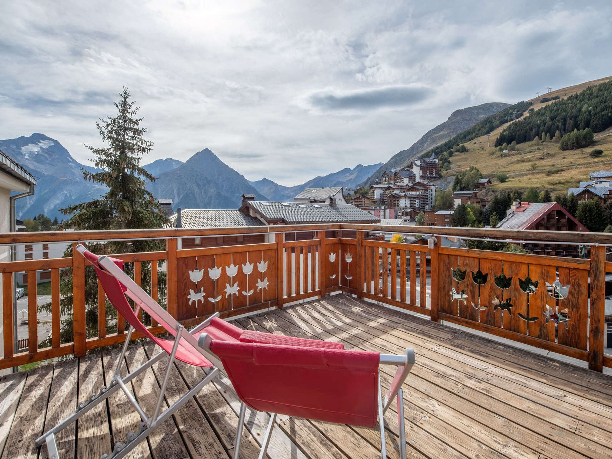 A wooden deck with a red chair, overlooking a mountainous landscape with buildings.