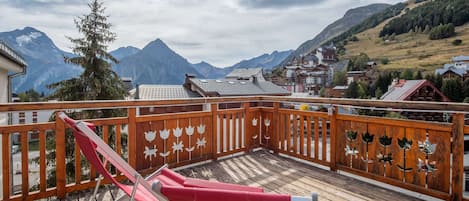 A wooden deck with a red chair, overlooking a mountainous landscape with buildings.