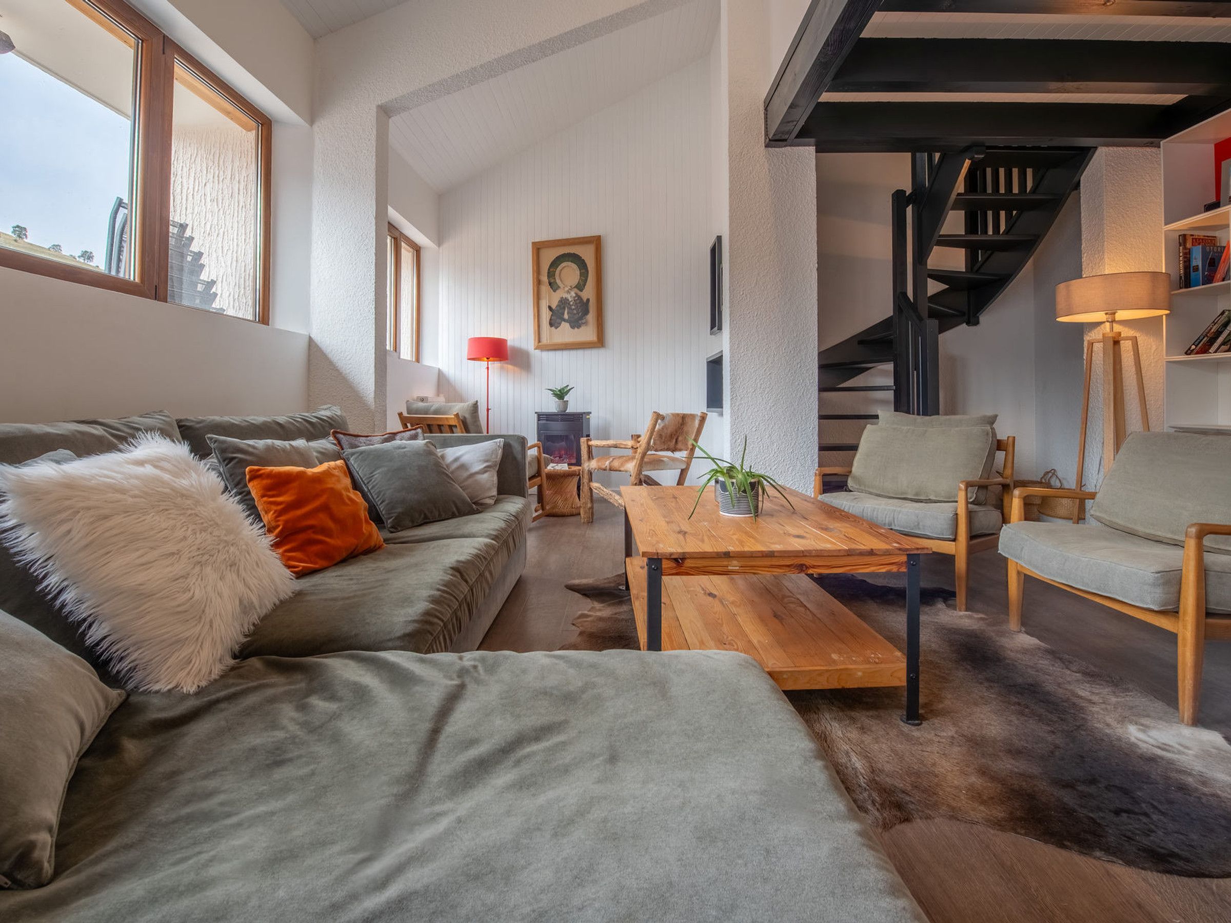 Una sala de estar moderna con un sofá, sillas, una mesa de centro de madera y una escalera.
