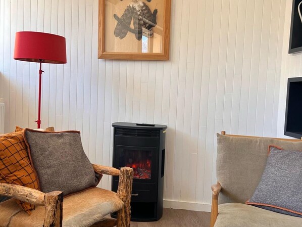 Una sala de estar acogedora con una chimenea de leña, una lámpara roja de pie y dos sillones.