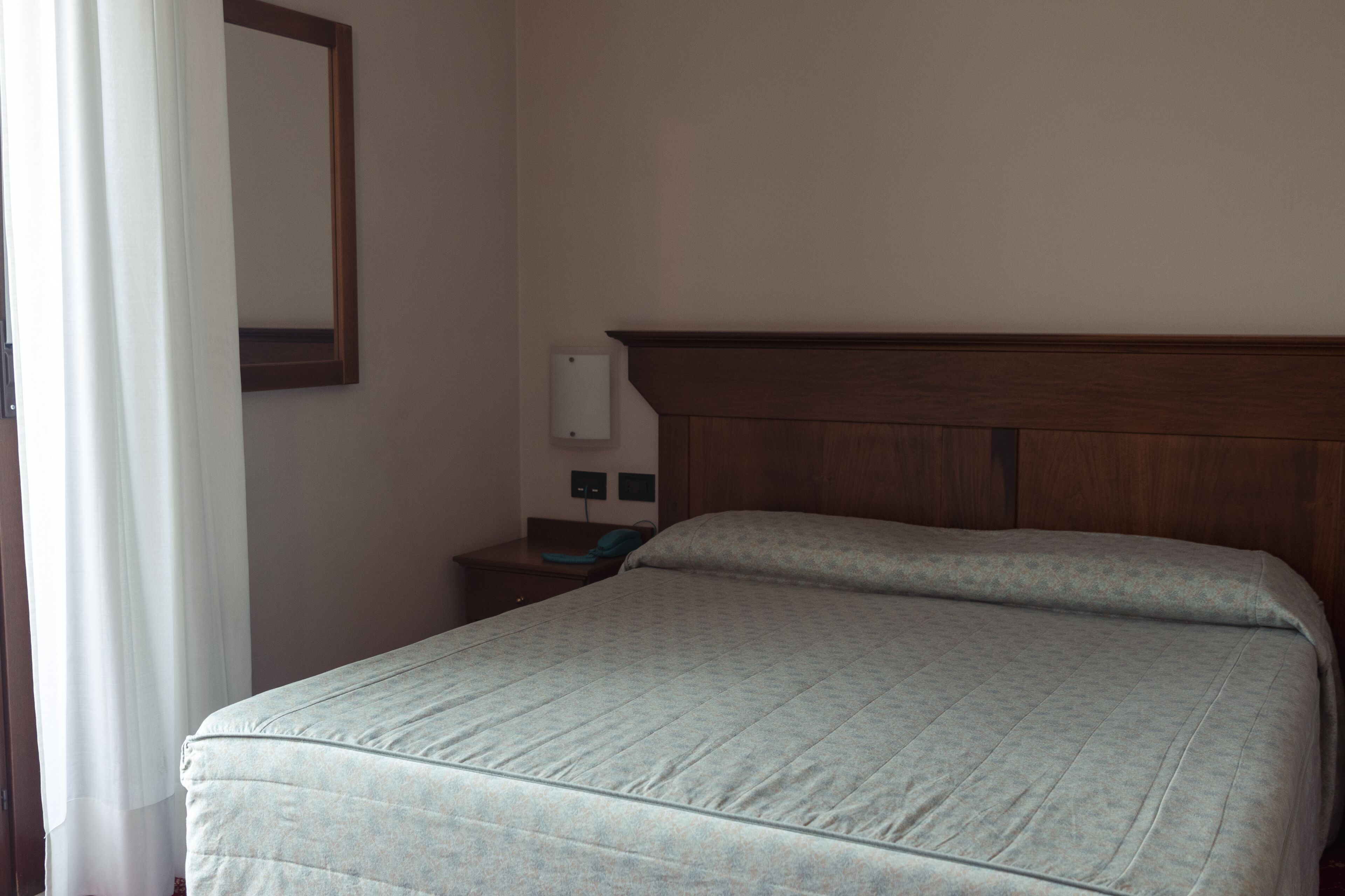 Habitación de hotel con una cama individual, una mesita de noche, un espejo e interruptor de luz en la pared.