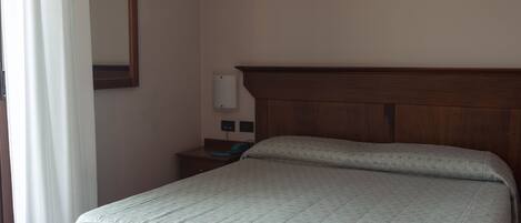 Habitación de hotel con una cama individual, una mesita de noche, un espejo e interruptor de luz en la pared.