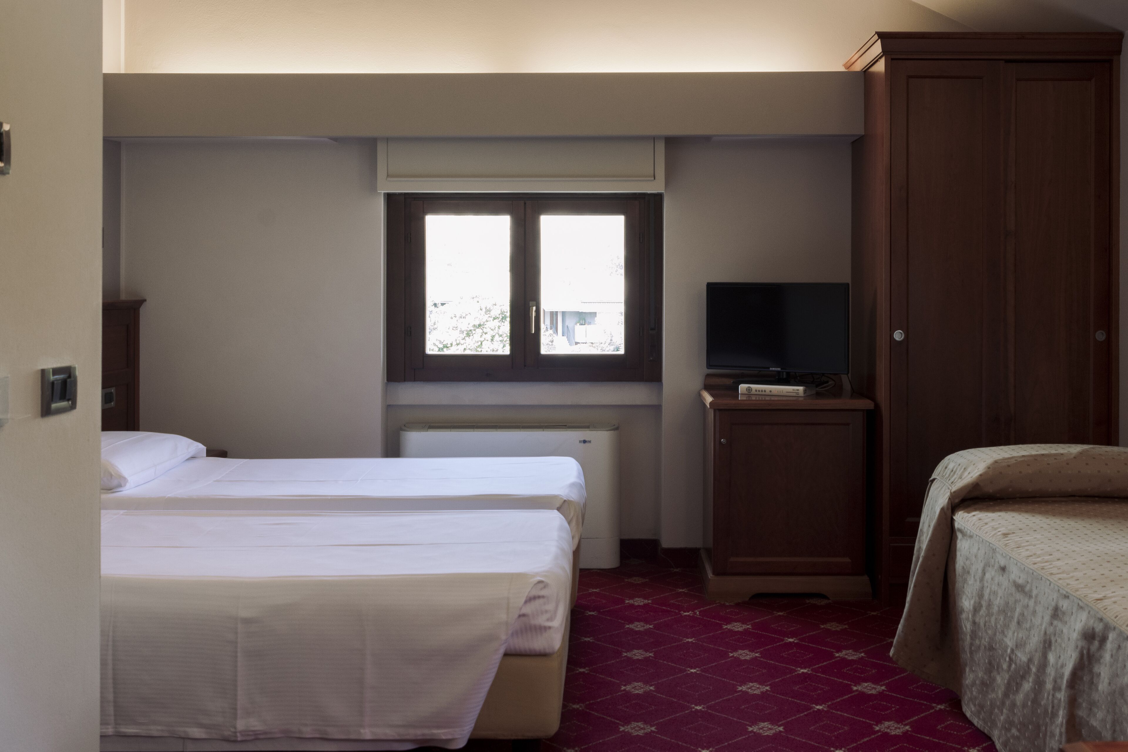 Une chambre d’hôtel avec deux lits, une télévision, une armoire et une fenêtre avec des stores.