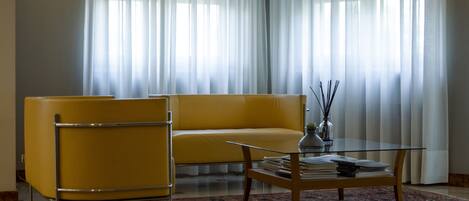 A modern living room with a yellow sofa, a glass coffee table, and a patterned rug.