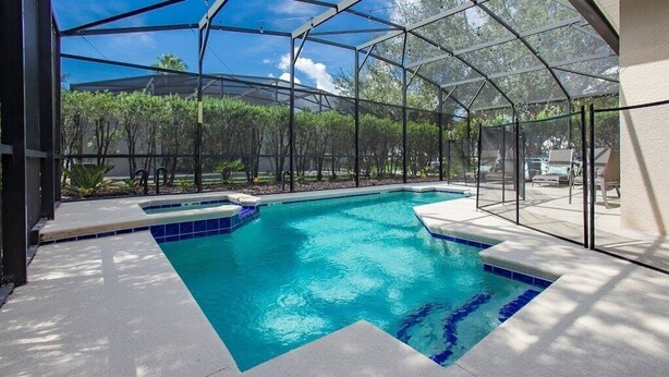 En swimmingpool med et glasindhegning, omgivet af en terrasse med liggestole.
