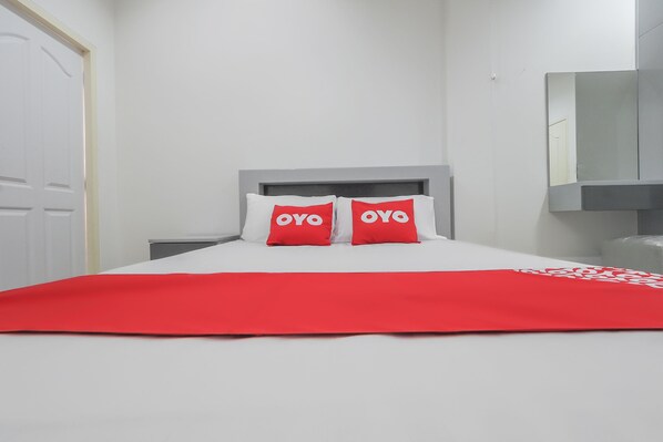 Una habitación de hotel con una cama, dos almohadas rojas con el logotipo 'OYO', una colcha roja, un cabecero gris y una puerta blanca.