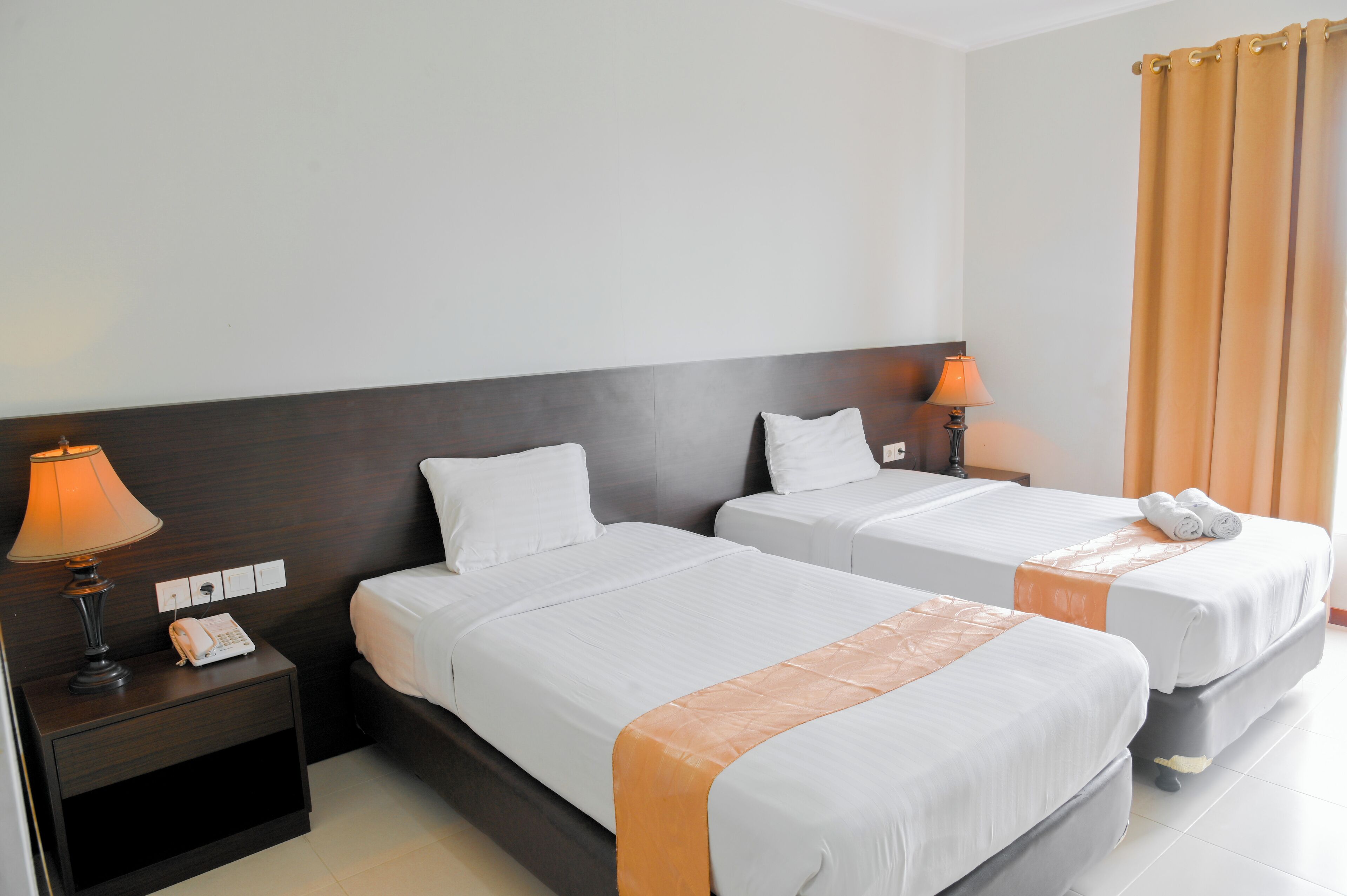 A hotel room with two beds, a nightstand with a lamp, and a telephone.