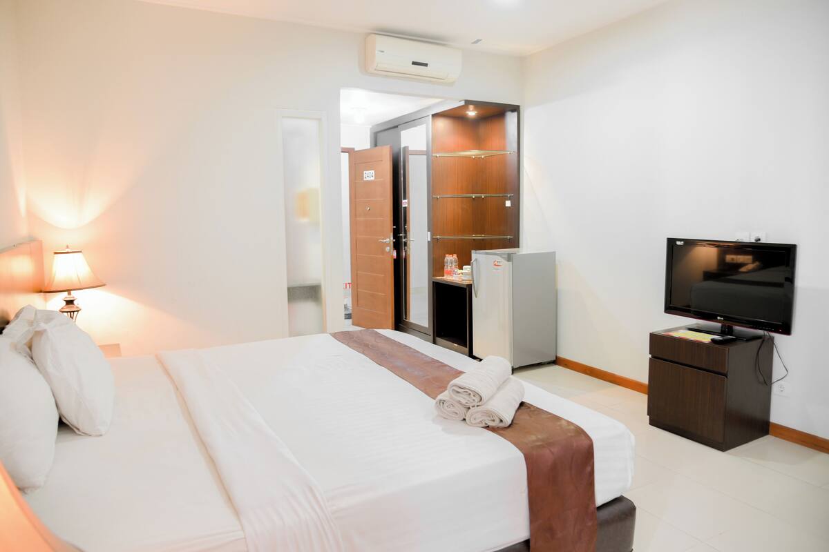 A hotel room with a bed, a television, a wardrobe, and a desk.