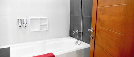 Un baño con una bañera blanca, una toalla roja, un cabezal de ducha y una puerta de madera.
