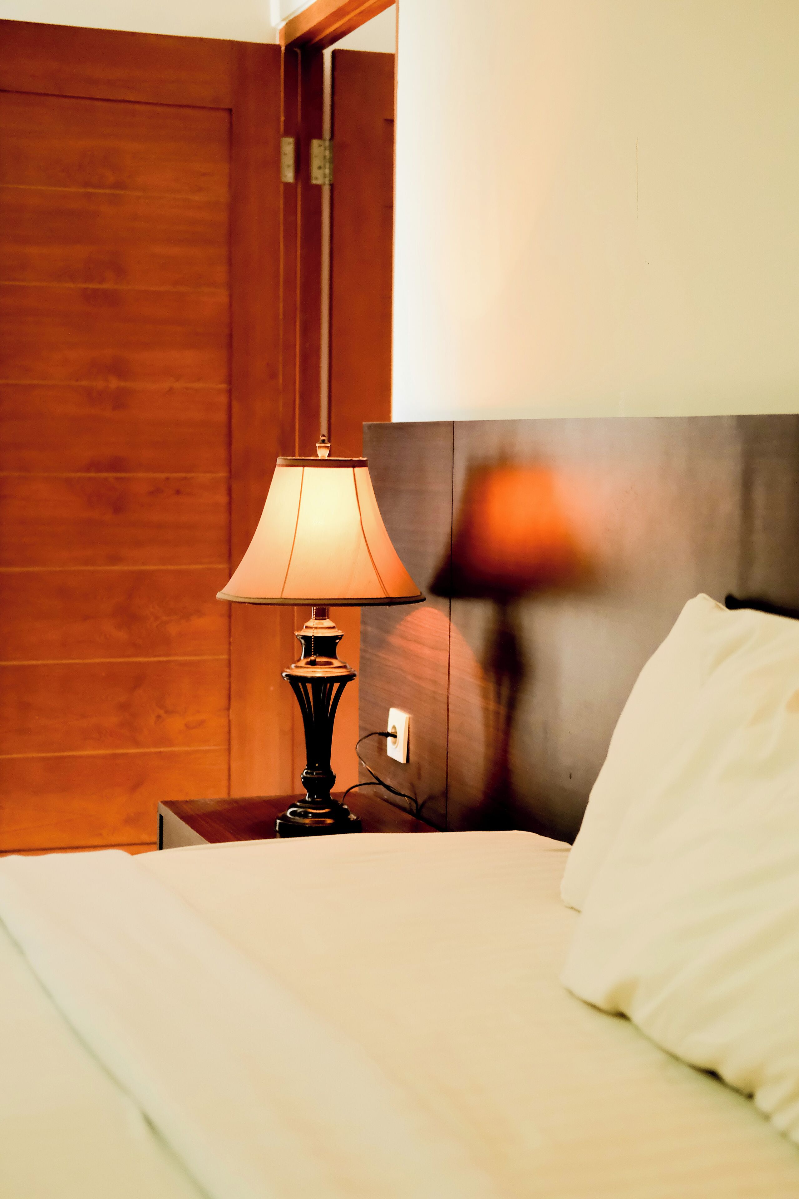 A hotel room with a wooden headboard, a bedside lamp, and a white bed.