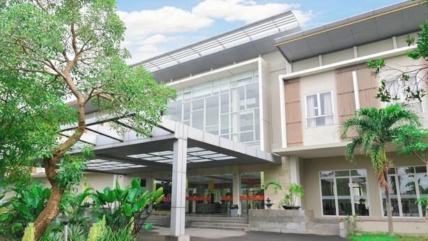 A modern building with a covered entrance, large windows, and a well-maintained garden with various plants.