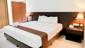 A hotel room with a large bed, two bedside tables with lamps, a wooden headboard, and a door with curtains.