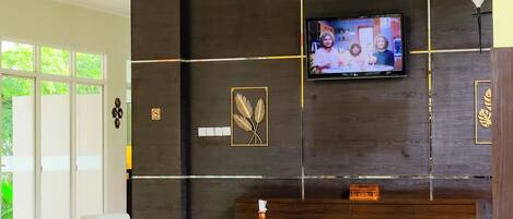 A modern living room with a flat-screen TV mounted on a dark wooden wall, two grey sofas, and a white tiled floor.