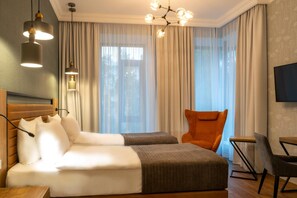A hotel room with a bed, two bedside tables, a chair, a TV, and a window with curtains. - Botanica Hotel (Arkhangelsk)