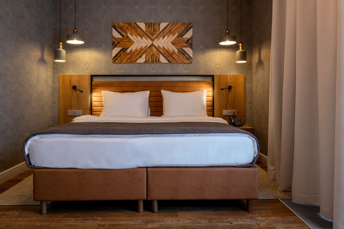 A large bed with a wooden headboard, two bedside tables, and a wall-mounted artwork above.