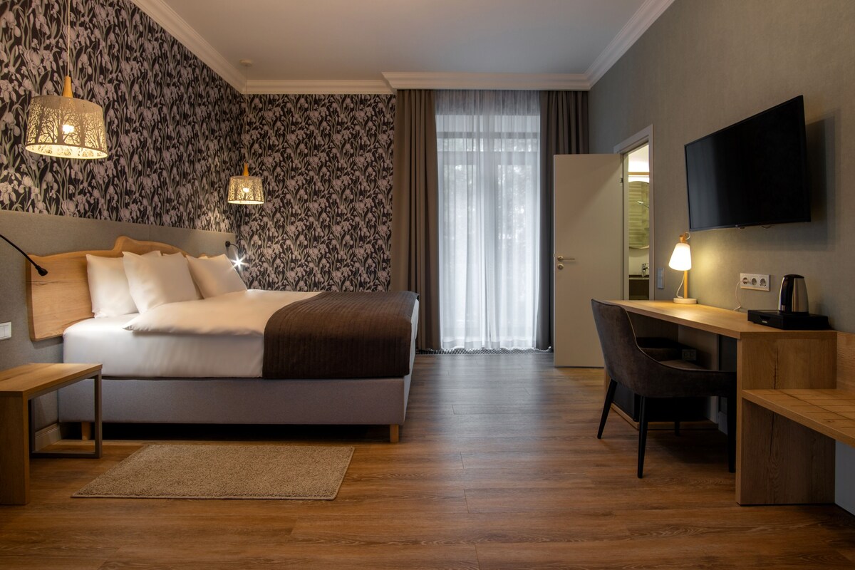 A modern hotel room with a large bed, a desk, a chair, and a TV.