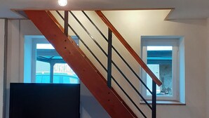 Ein modernes Wohnzimmer mit Treppe, Essbereich mit Tisch und Stühlen, Flachbildfernseher und Fenster mit Blick.