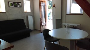 Ein Zimmer mit einer schwarzen Couch, einem runden Tisch mit Stühlen, einem Heizkörper und einem Fenster mit Blick auf Grünfläche.