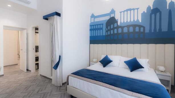 A hotel room with a bed, a nightstand, a wall mural of famous buildings, and a door leading to another room. - Frattina FF (Rome)