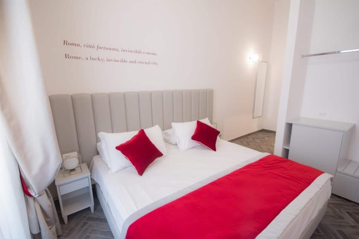 Una habitación de hotel moderna con una cama grande, ropa de cama blanca y detalles en rojo.