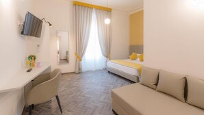 A hotel room with a bed, a sofa, a desk with a chair, a TV, and a window with curtains. - Frattina FF (Rome)
