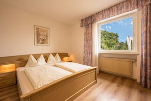 Un dormitorio con cama de madera, una ventana con cortinas, un radiador y un cuadro enmarcado en la pared.