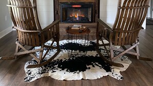 A cozy living room with a fireplace, two wooden chairs, a cowhide rug, and a mirror above the fireplace.