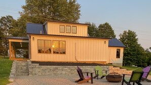 A modern house with a stone staircase leading to a porch, outdoor seating with Adirondack chairs, and a fire pit.