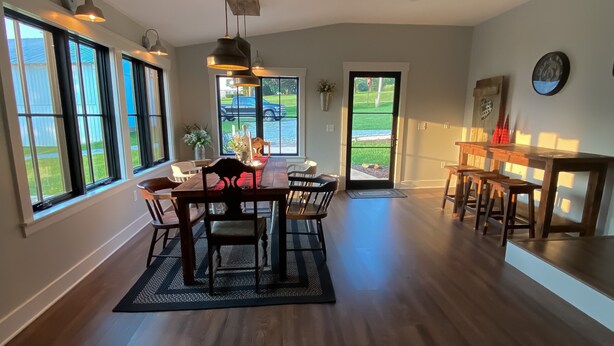 A spacious dining area with a wooden table and chairs, large windows, and a view of the outdoors.