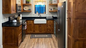 A kitchen with wooden cabinets, a stainless steel refrigerator, and a window with a view of trees.