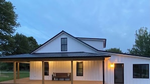 A modern single-story house with a covered porch, a small deck, and a well-maintained lawn.