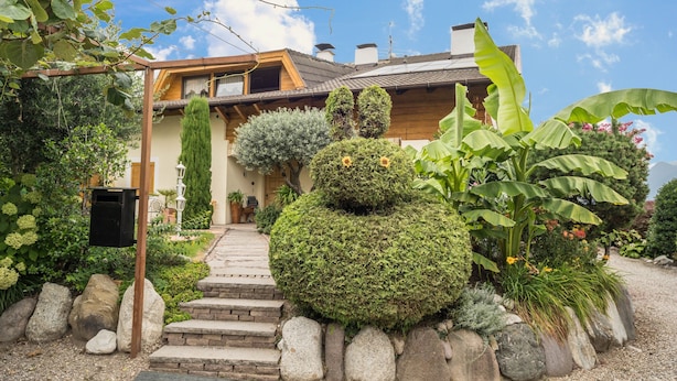 A house with a stone pathway leading to the entrance, surrounded by various plants and a well-maintained garden. - Apartment "Residenz Kronstein - 3" with Balcony, Shared Garden, Mountain View & Wi-Fi (Tisens)