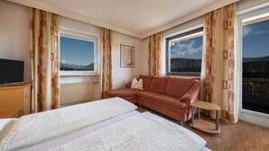 A hotel room with a bed, a sofa, a TV, and large windows with curtains. - Apartment "Residenz Kronstein - 3" with Balcony, Shared Garden, Mountain View & Wi-Fi (Tisens)