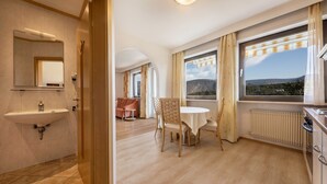 A modern hotel room with a bathroom, a dining area with a table and chairs, and a large window with a mountain view. - Apartment "Residenz Kronstein - 3" with Balcony, Shared Garden, Mountain View & Wi-Fi (Tisens)