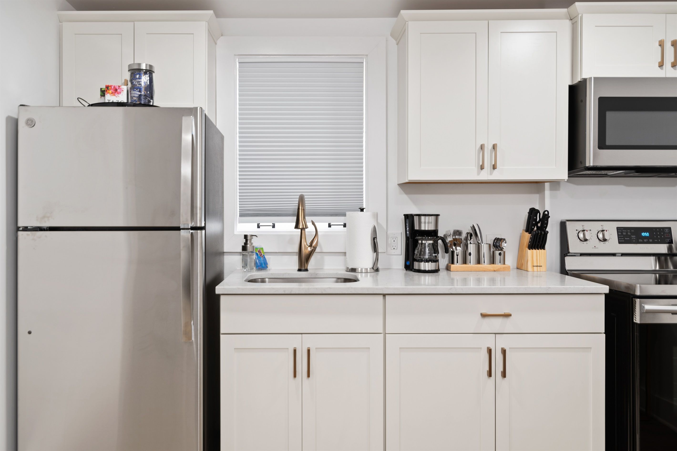 Una cocina moderna con armarios blancos, electrodomésticos de acero inoxidable y una ventana con persianas.