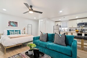 A modern living room with a teal sofa, a bed with white bedding, and a kitchen in the background. - Hillsboro Village Studio · Free Parking, No Stairs · Walk to Vandy & Belmont (Nashville)