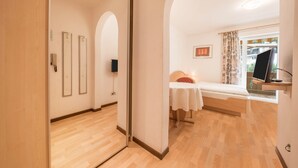 Un dormitorio con cama, una mesita, un televisor y un ventanal con cortinas.