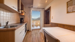 A compact kitchen with a sink, stove, and cabinets, leading to a balcony with a view of mountains. - Apartment "Residenz Kronstein - 5" with Balcony, Garden, Mountain View & Wi-Fi (Tisens Italien)