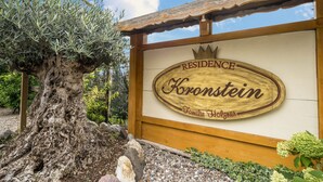 A wooden sign with 'RESIDENCE Kronstein' and 'Familie Holzner' written on it, set against a backdrop of a large tree and a clear sky. - Apartment "Residenz Kronstein - 5" with Balcony, Garden, Mountain View & Wi-Fi (Tisens Italien)