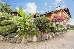A two-story building with a balcony, surrounded by a well-maintained garden with various plants and a gravel path.