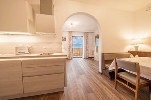 A modern kitchen with wooden cabinets, a dining area with a table and bench, and an arched doorway leading to a balcony.