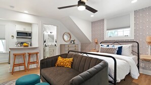 Un dormitorio moderno con cama, ventilador de techo, kitchenette y baño.