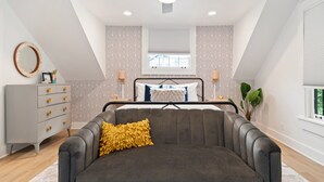 Un dormitorio con cama, sofá gris, ventilador de techo, cómoda y papel tapiz estampado.