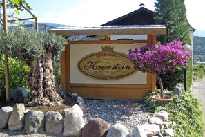 A sign for 'RESIDENCE Kronstein' with a rustic wooden structure, a bonsai tree, and a flowering plant. - Apartment "Residenz Kronstein - 7" with Balcony, Shared Garden and Mountain View (Tisens Italien)