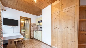 Een kamer met houten plafond, een keuken met kastjes, een eettafel en een televisie aan de wand.