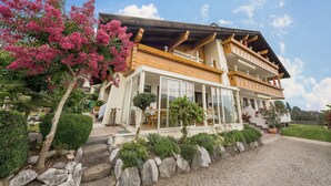 Een chalet met twee verdiepingen, een balkon, een overdekte veranda en een keurig onderhouden tuin.