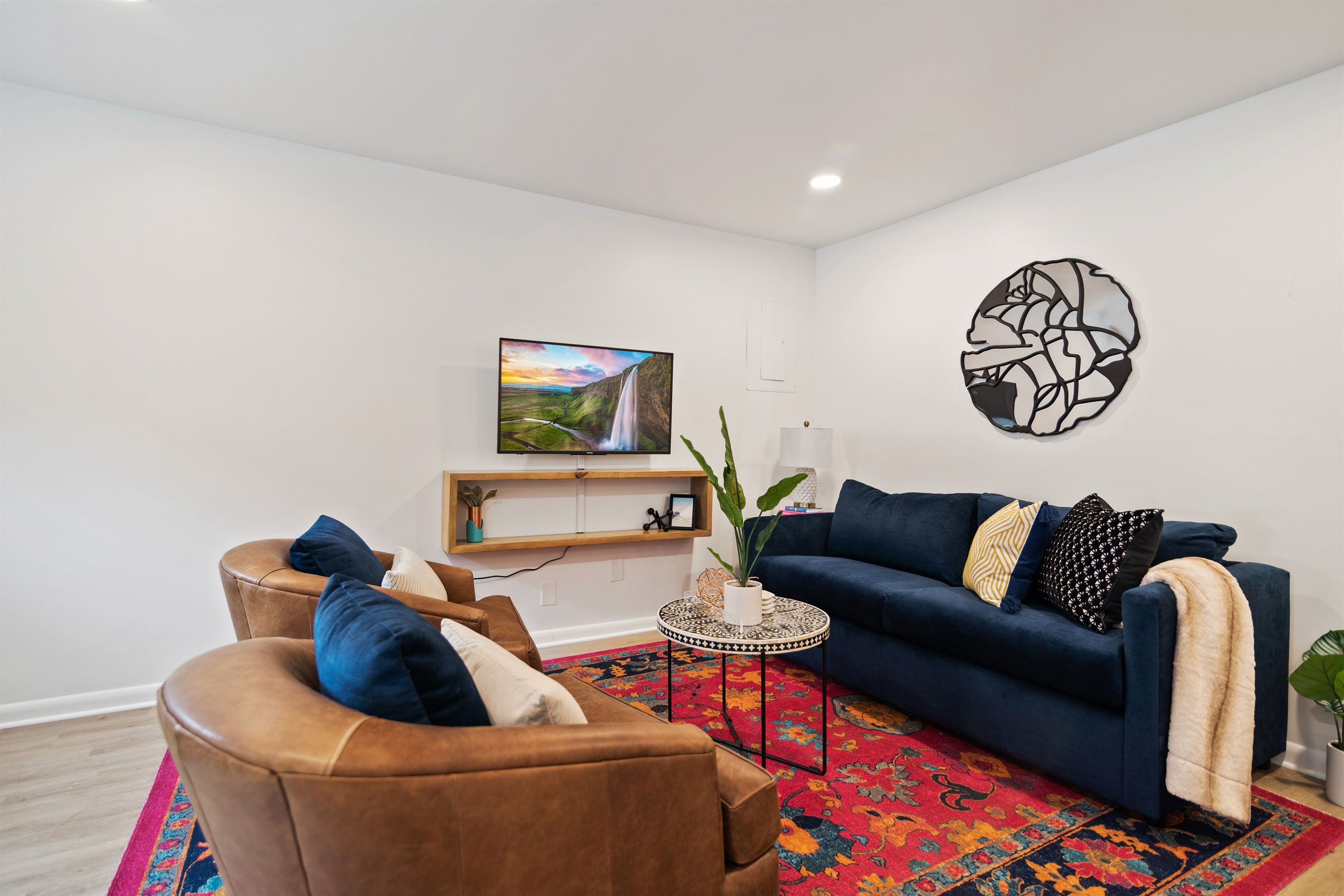 Un salon avec un canapé bleu, un fauteuil en cuir marron et une petite table ronde sur laquelle est posée une plante.