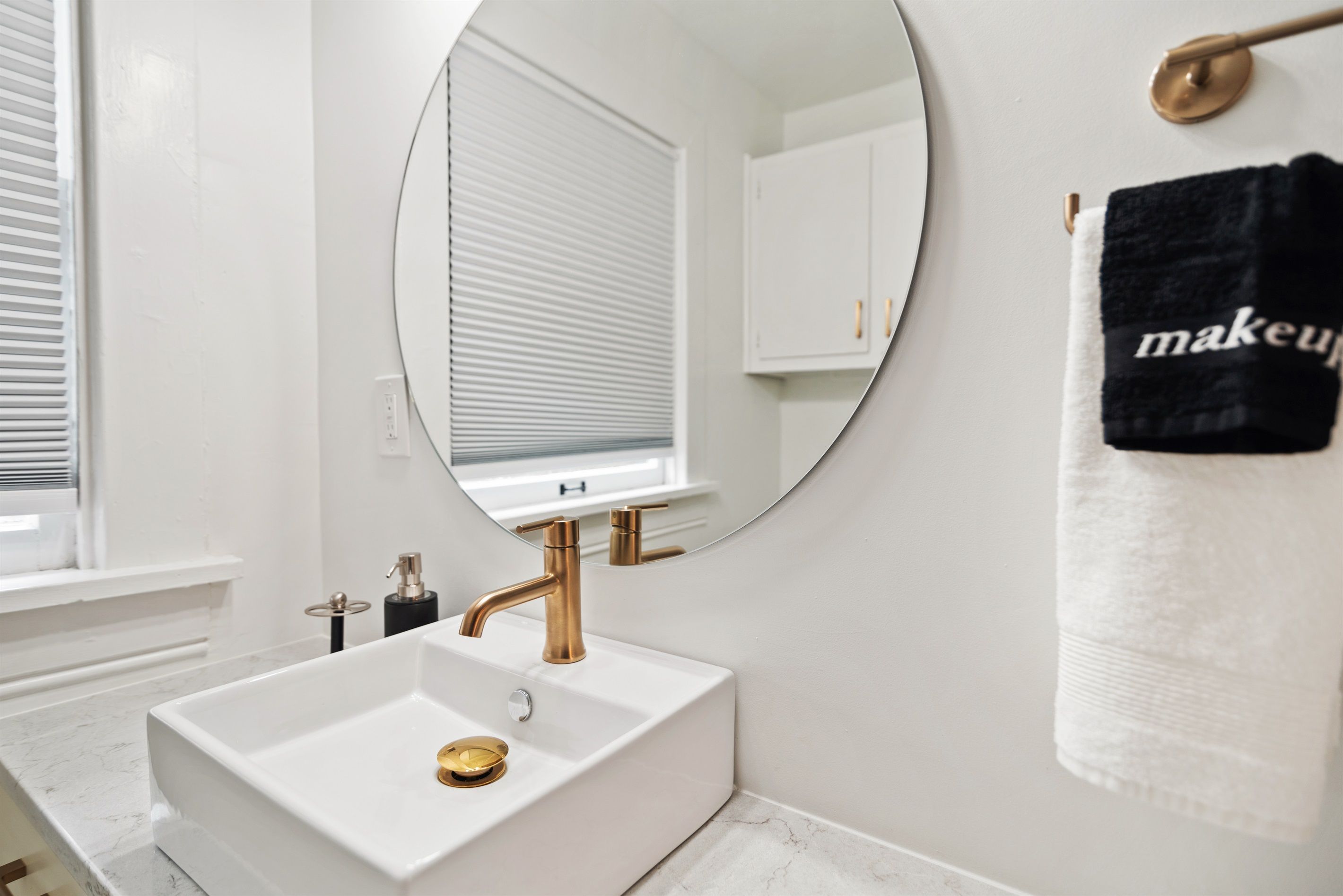 A bathroom with a white sink, gold faucet, and a round mirror.