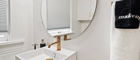 A bathroom with a white sink, gold faucet, and a round mirror.